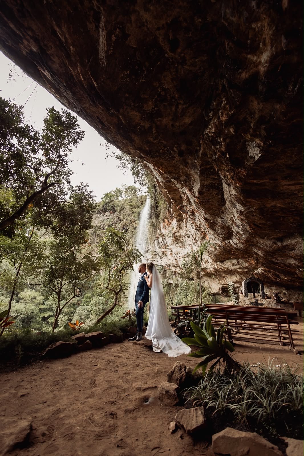 Casal sob uma gruta de pedra com cachoeira ao fundo